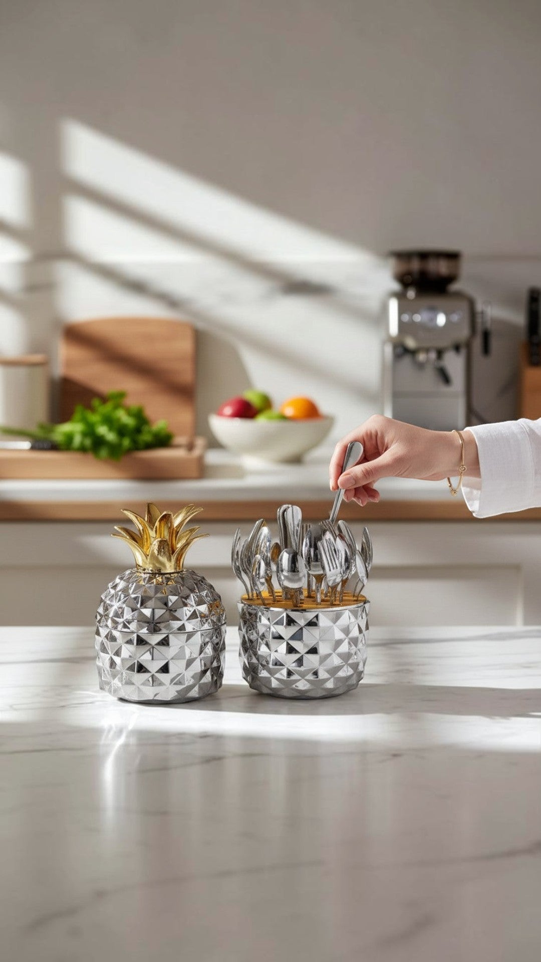 Set de cubiertos Castor UP de acero inoxidable con soporte decorativo en forma de piña plateada sobre mesa de mármol